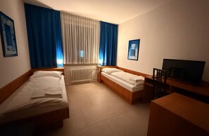 A hotel room with two beds, a desk, a chair, a television, and a window with curtains. - Hotel G&k (Giesen)