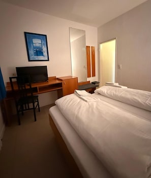 A hotel room with a bed, a desk, a chair, a television, and a mirror. - Hotel G&k (Giesen)