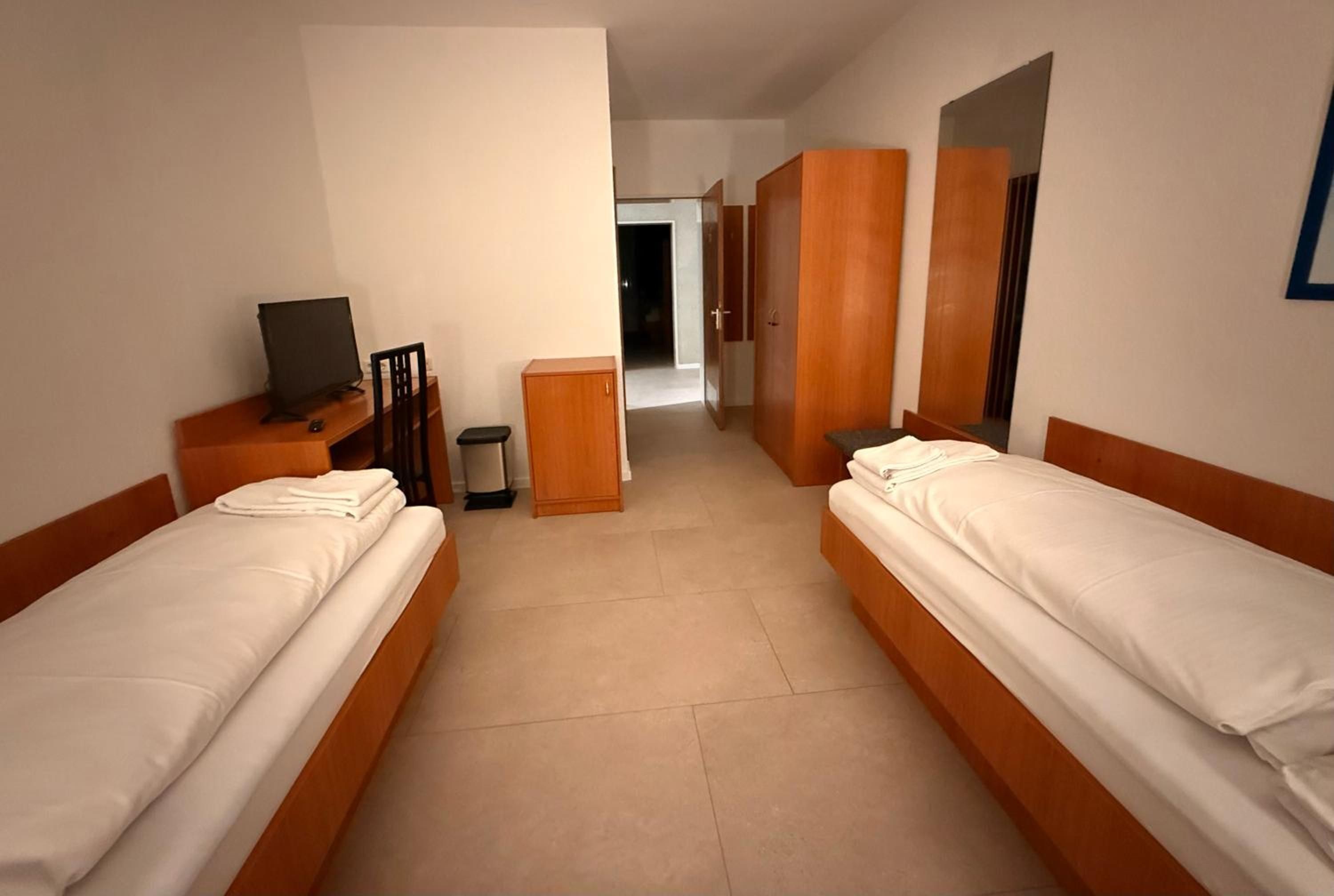 A hotel room with two single beds, a desk with a computer, a wardrobe, and a mirror.