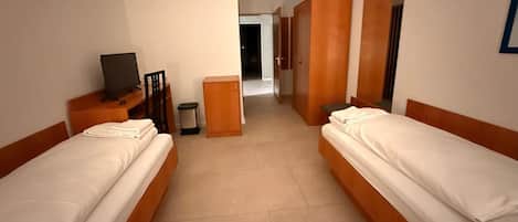 Una habitación de hotel con dos camas individuales, un escritorio con computadora, un armario y un espejo.