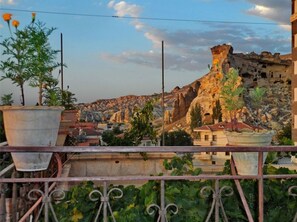Un balcón con barandilla, plantas en macetas y vista a un paisaje rocoso con edificios al fondo.