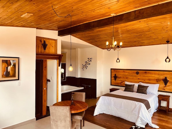 Ein Hotelzimmer mit Holzbalkendecke, einem Bett mit weißer Bettwäsche, einem Esstisch mit Stühlen und einer Kristallleuchtre.