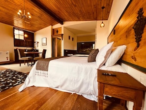 Ein Schlafzimmer mit einem großen Bett, einem Holz-Kopfteil, einem Schreibtisch mit Stuhl, einem Fernseher und einer Küchenzeile.
