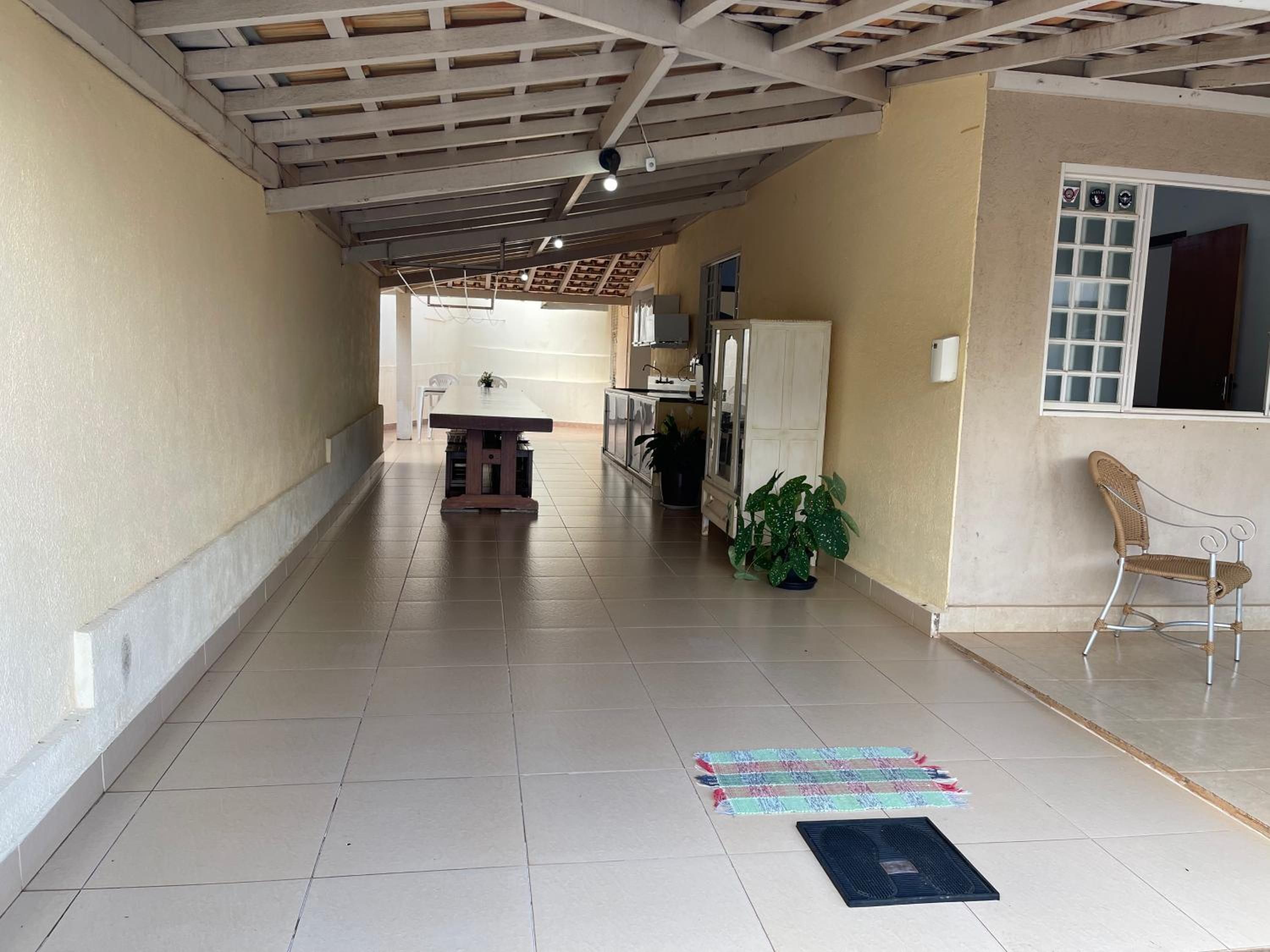 Um corredor com piso de azulejos, uma mesa de jantar, um vaso de planta, uma cadeira e uma janela com vista.