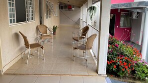 Een overdekt terras met rieten stoelen en een plant in pot.