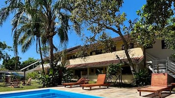 Piscina com água azul cristalina, cercada por espreguiçadeiras e palmeiras, com um edifício ao fundo.