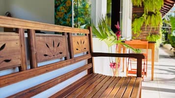 Um banco de madeira com design moderno, posicionado numa varanda com vista para um jardim e uma área de refeições.