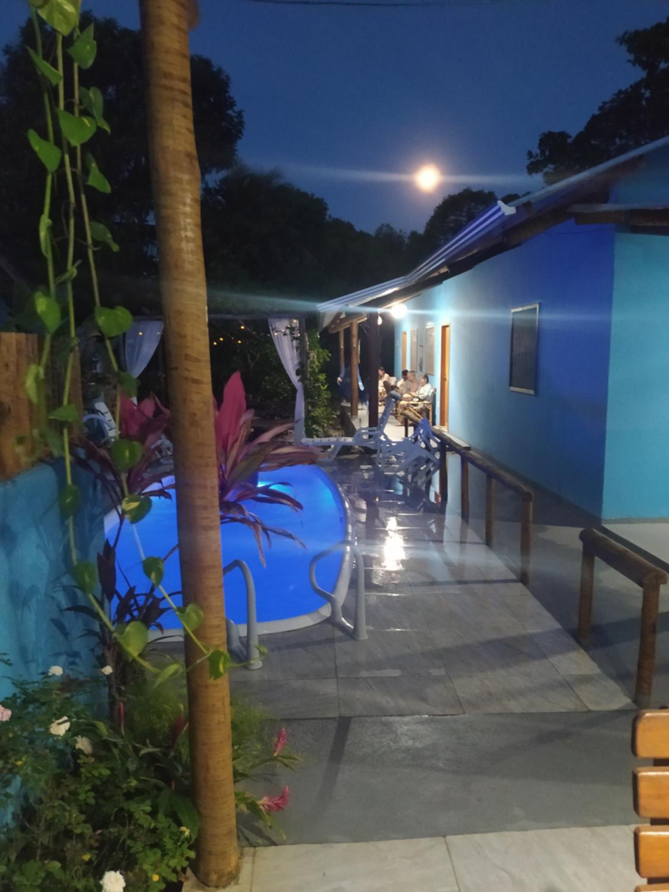 Área externa com piscina, área de estar e um edifício com fachada azul.