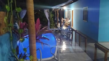 Área externa com piscina, área de estar e um edifício com fachada azul.