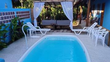 Piscina com espreguiçadeiras brancas e área de estar coberta.