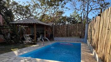 Piscina com ladrilhos de pedra, duas espreguiçadeiras e um cercado de bambu.