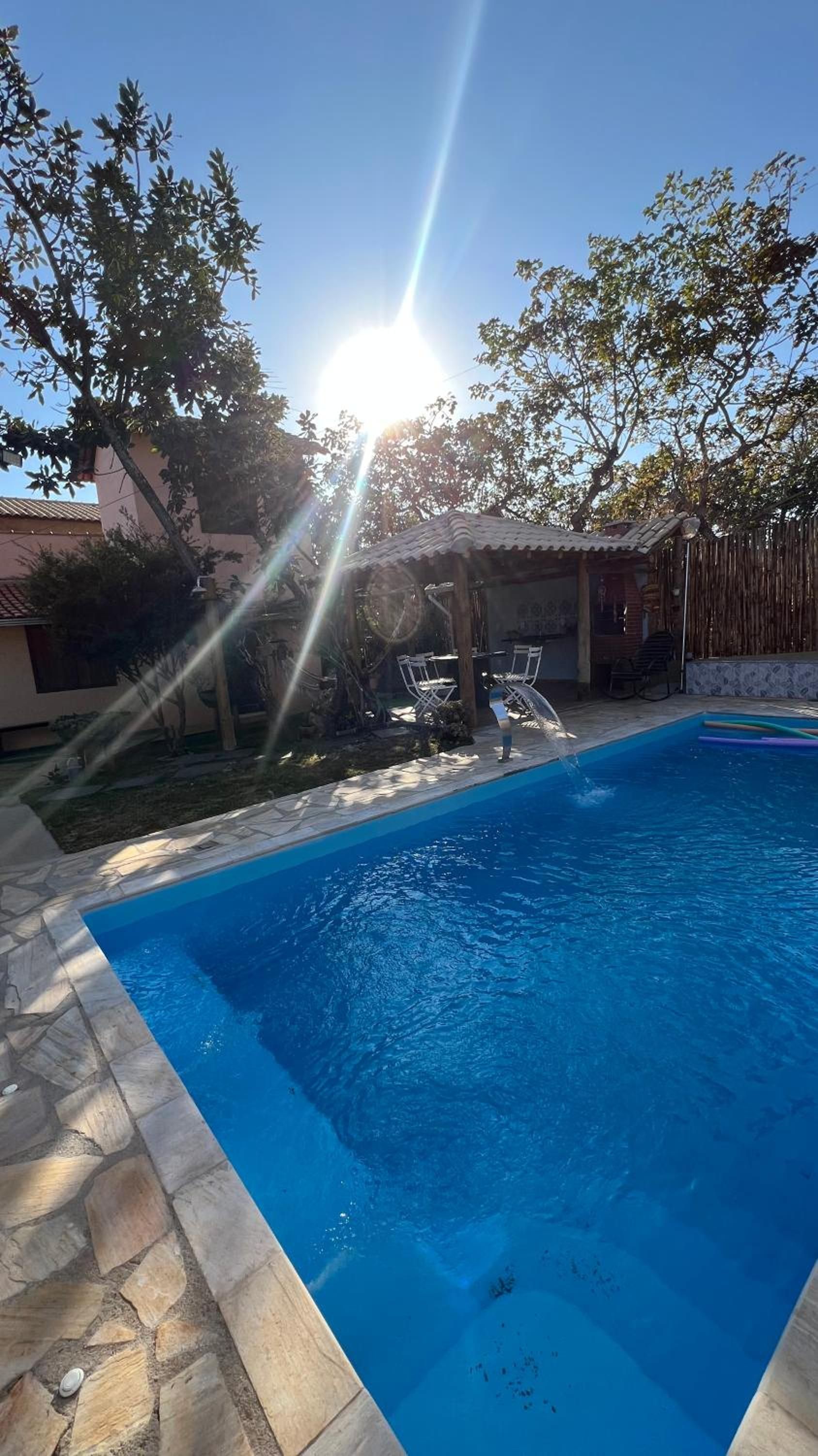 Piscina com ladrilhos de pedra, cercada por um jardim e um edifício.