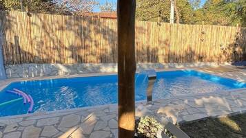 Área de varanda coberta com piscina, piso de pedra e um banco de metal branco.