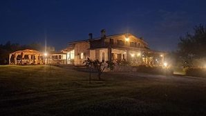 A large, illuminated building with a prominent entrance and a covered outdoor area. - Villa Klinai (Cerveteri)