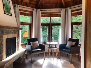 Una habitación acogedora con chimenea, dos sofás, una mesita y ventanas amplias con cortinas.