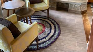 Een knusse woonkamer met een open haard, een bank, een rond bijzettafeltje en een kleurrijk vloerkleed.