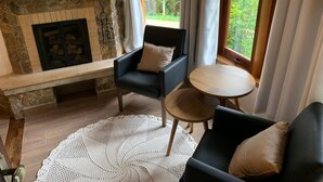 Een gezellige woonkamer met een open haard, twee fauteuils, een ronde salontafel en uitzicht op groen.