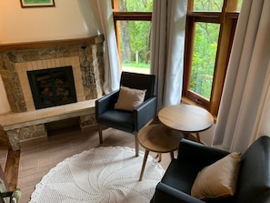 Una sala de estar acogedora con chimenea, dos sillones, una mesa de centro redonda y vistas al exterior.