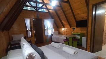 Um quarto de sótão aconchegante, com teto inclinado, cama com almofadas, mesa pequena e televisão na parede.