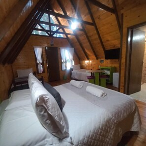 Um quarto de sótão aconchegante, com teto inclinado, cama com almofadas, mesa pequena e televisão na parede.
