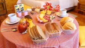 A breakfast buffet with various food items and a bed in the background. - Estalagem Refúgio Do Capão (Cambara do Sul)