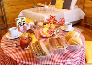 Buffet de café da manhã com diversos alimentos e uma cama ao fundo.