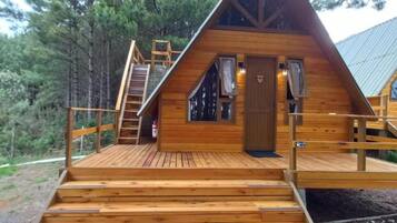 Uma cabana de madeira com telhado inclinado e um deck, com escadas que levam à entrada.