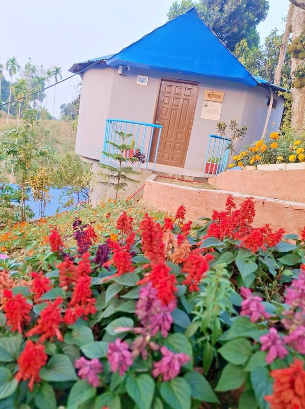 A small building with a blue roof and a door, surrounded by a garden with various flowers.