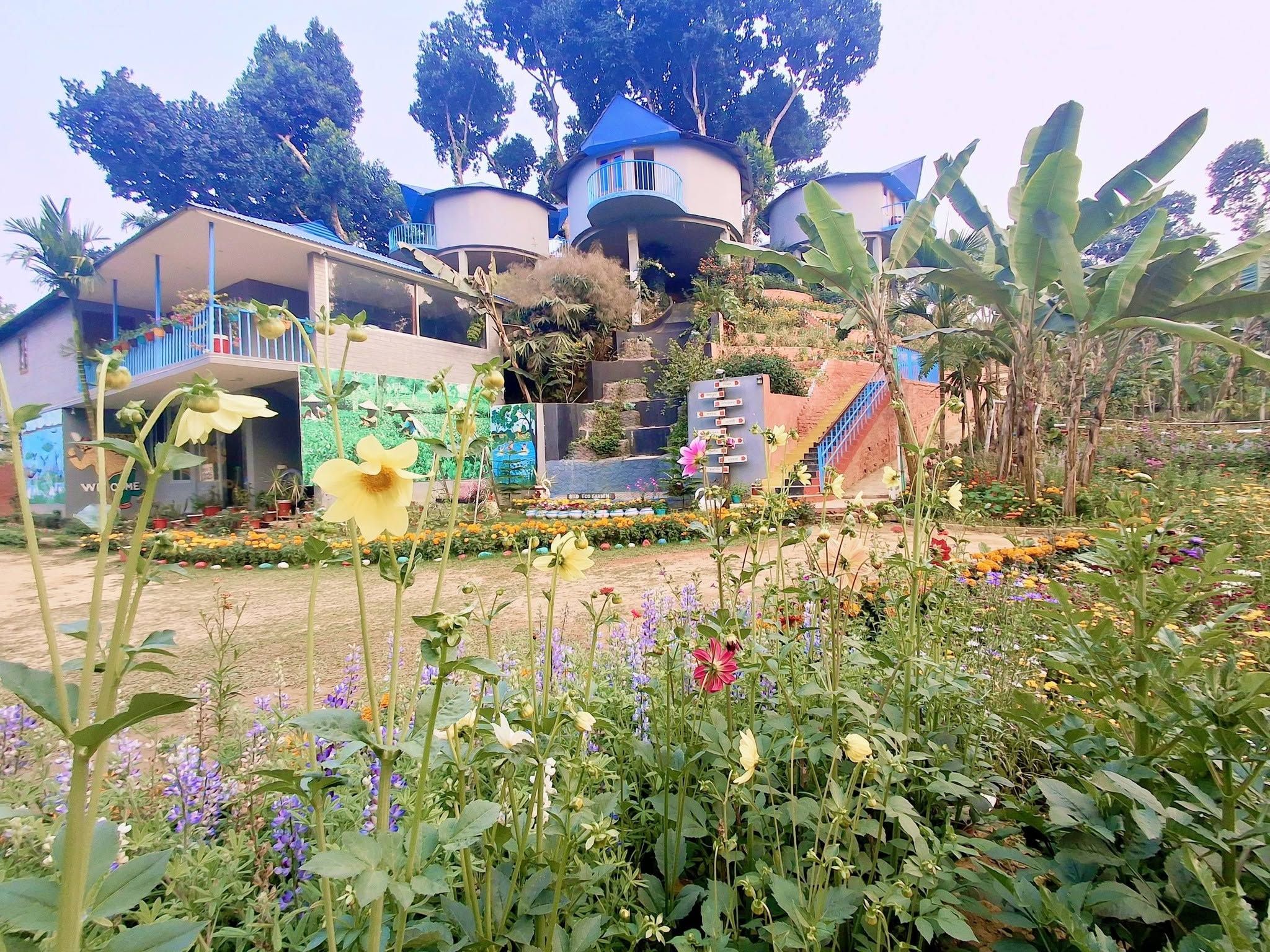 A garden with various flowers and plants, a building with a blue roof, and a staircase leading up to a balcony.