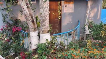 A building with a corrugated metal roof, surrounded by a variety of flowering plants and trees.