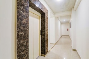 A hallway with a marble door, white walls, and a tiled floor.
