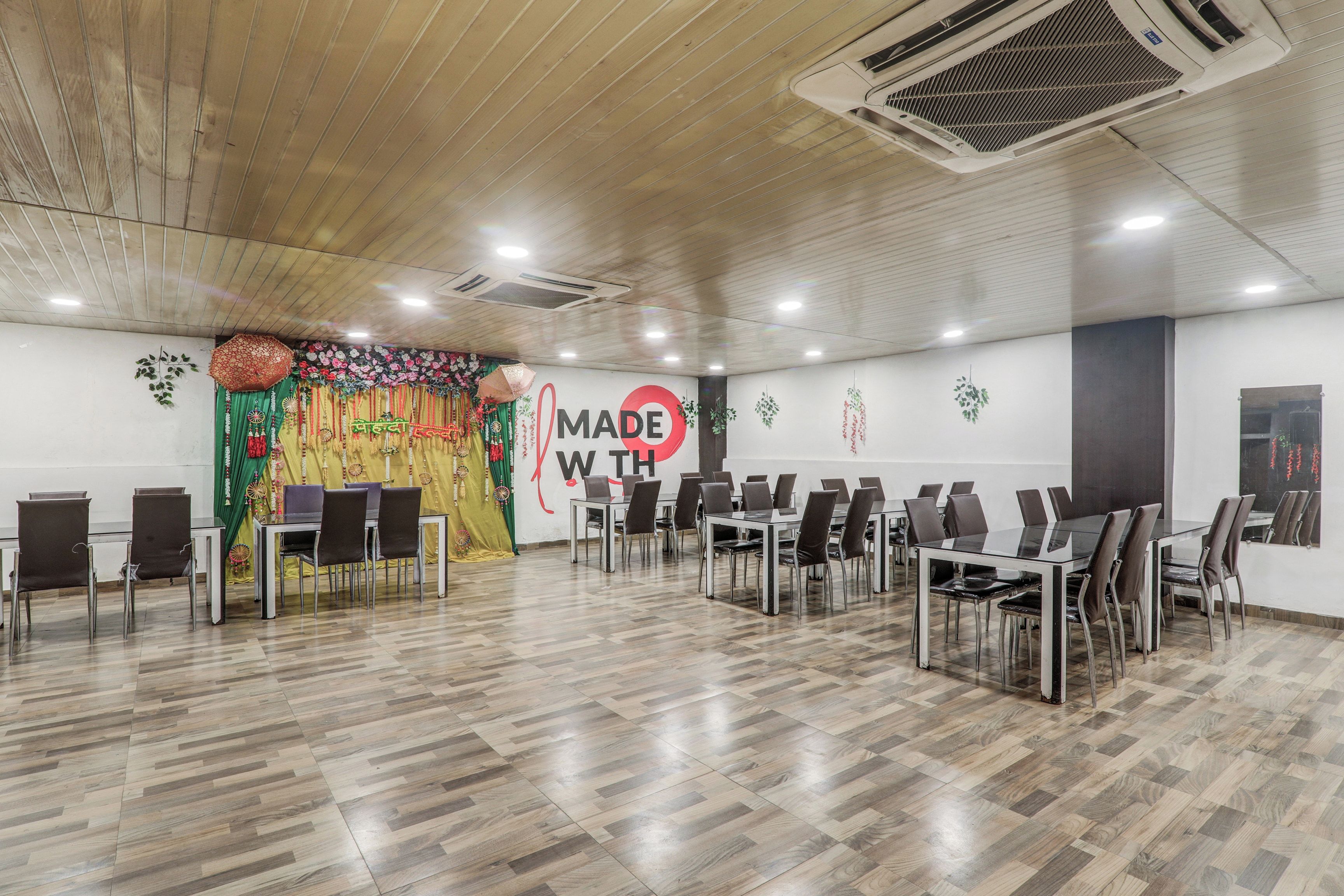 A conference room with a wooden ceiling, multiple tables and chairs, and a decorative backdrop with the text 'MADE WITH'.