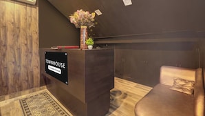 Ein Empfangsschalter mit einem Schild, das auf betriebseigene Dienstleistungen hinweist, ein Holzboden, ein gemustertes Teppich und ein Ledersofa mit Kissen.
