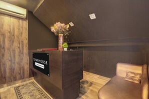 A reception desk with a sign indicating it is company-serviced, a wooden floor, a patterned rug, and a leather sofa with a pillow. - OYO Townhouse Awas Vikas Kalyanpur (Kanpur)