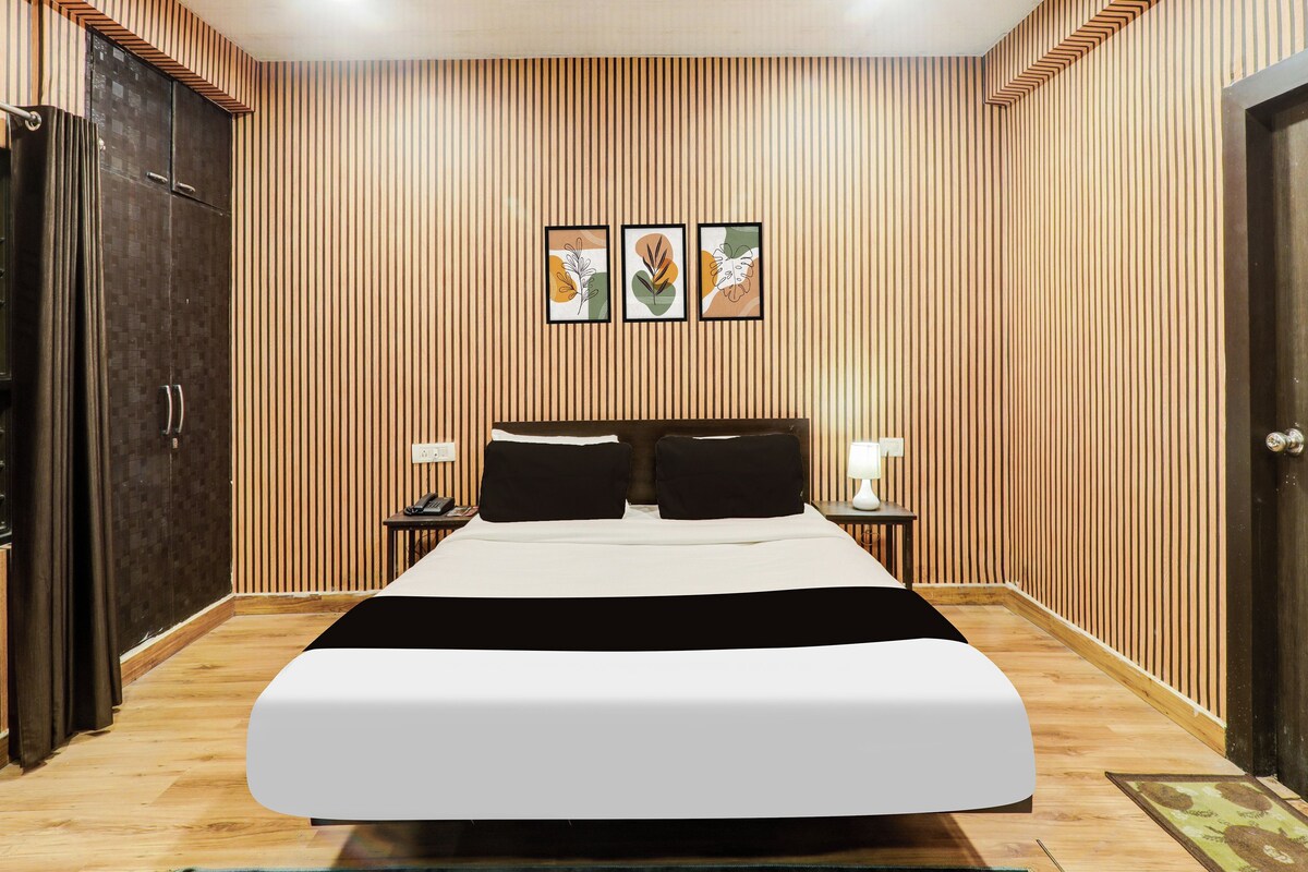 Quarto de hotel com uma cama grande, parede de ripas de madeira e porta à esquerda.