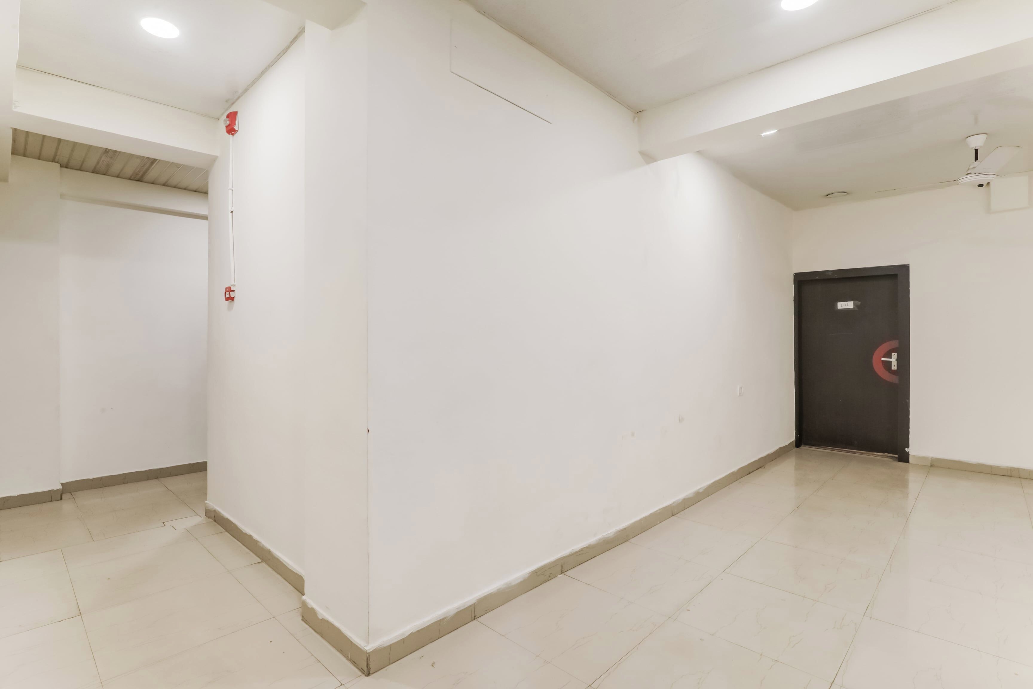 A corridor with white walls, a tiled floor, and a door with a red emergency exit sign.