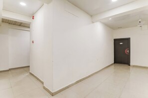 Um corredor com paredes brancas, piso ladrilhado e uma porta com placa de saída de emergência vermelha.