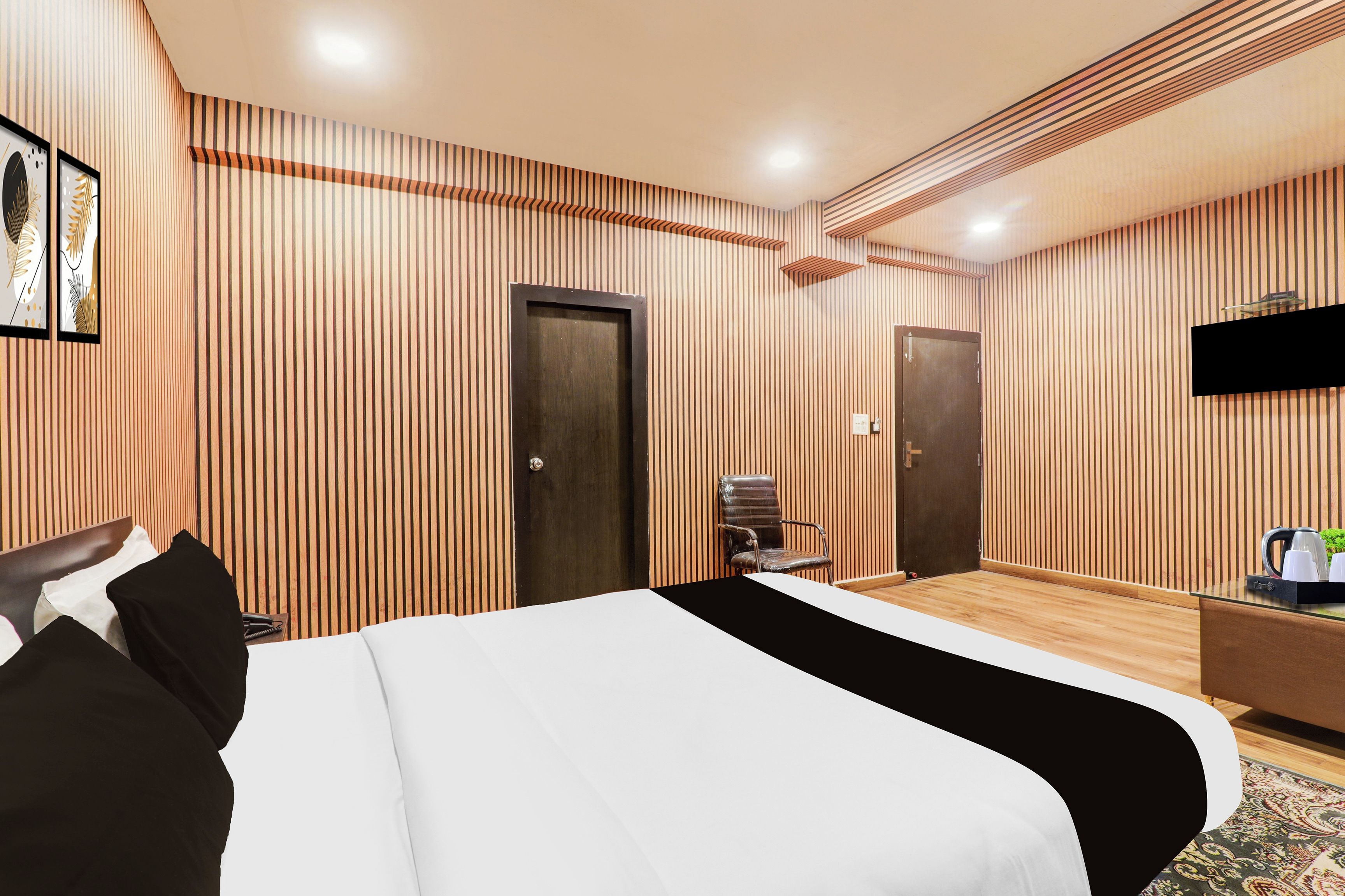 A hotel room with a large bed, two doors, a TV, and a small table with a kettle.