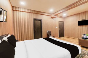 Quarto de hotel com uma cama grande, duas portas, uma TV e uma mesinha com chaleira.