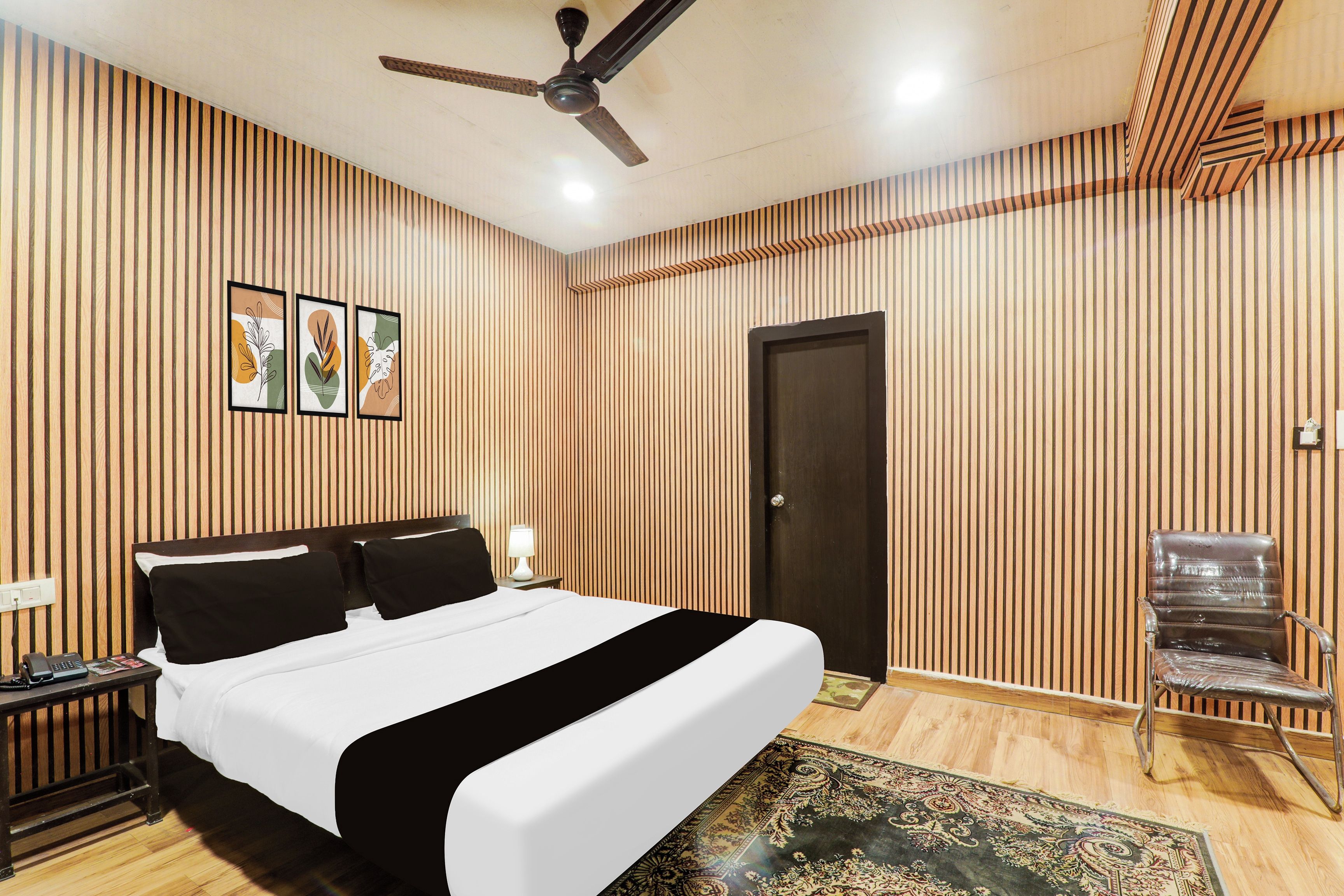 Habitación de hotel con cama, escritorio, silla, ventilador de techo y puerta.