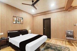 A hotel room with a bed, a desk, a chair, a ceiling fan, and a door. - OYO Townhouse Awas Vikas Kalyanpur (Kanpur)
