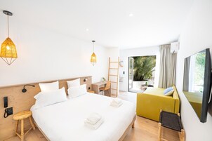 Una habitación de hotel moderna con una cama grande, un escritorio, una silla y un sofá. Se ve un ventanal con vistas a zonas verdes.