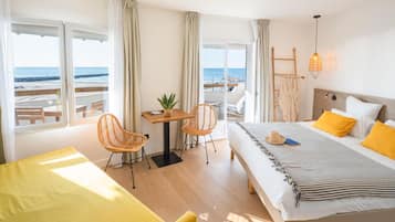 Een hotelkamer met een bed, een bureau, stoelen en uitzicht op het strand.