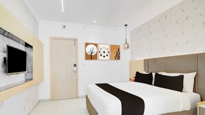 A hotel room with a bed, a TV mounted on the wall, a door, and artwork on the wall. - Townhouse Oak AECS Layout Brookfield (Bangalore)