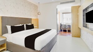 A modern hotel room with a large bed, a television mounted on the wall, and a view into the adjacent bathroom. - Townhouse Oak AECS Layout Brookfield (Bangalore)