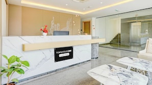 A hotel reception area with a marble reception desk, a potted plant, and a cityscape wall art. - Townhouse Oak AECS Layout Brookfield (Bangalore)