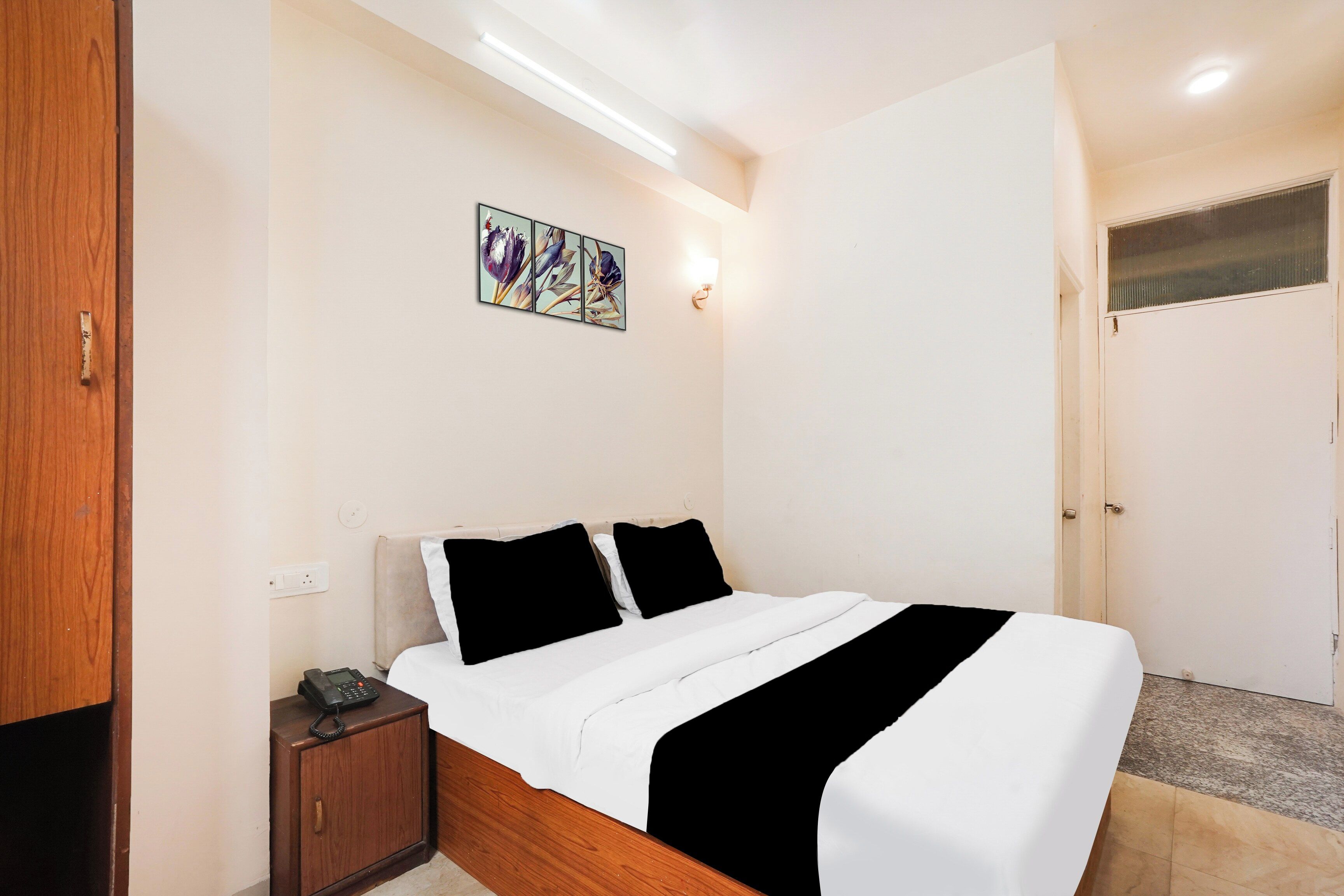 Quarto com cama, mesa de cabeceira, luminária na parede e uma porta.