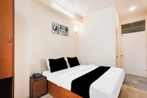 Quarto com cama, mesa de cabeceira, luminária na parede e uma porta.