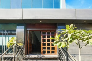 Entrada de un edificio con puerta de madera, escaleras metálicas y barandilla de metal.