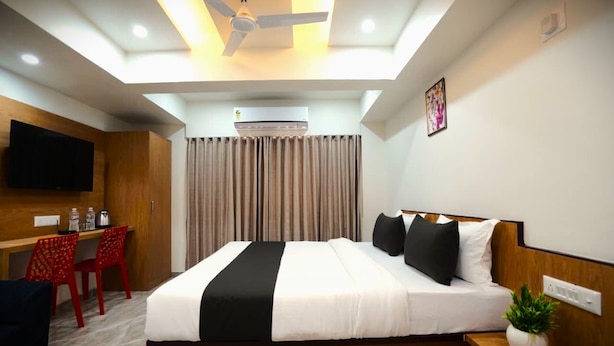 A hotel room with a bed, a desk, a chair, a ceiling fan, and an air conditioning unit. - hotel orange tree (Ahmedabad)